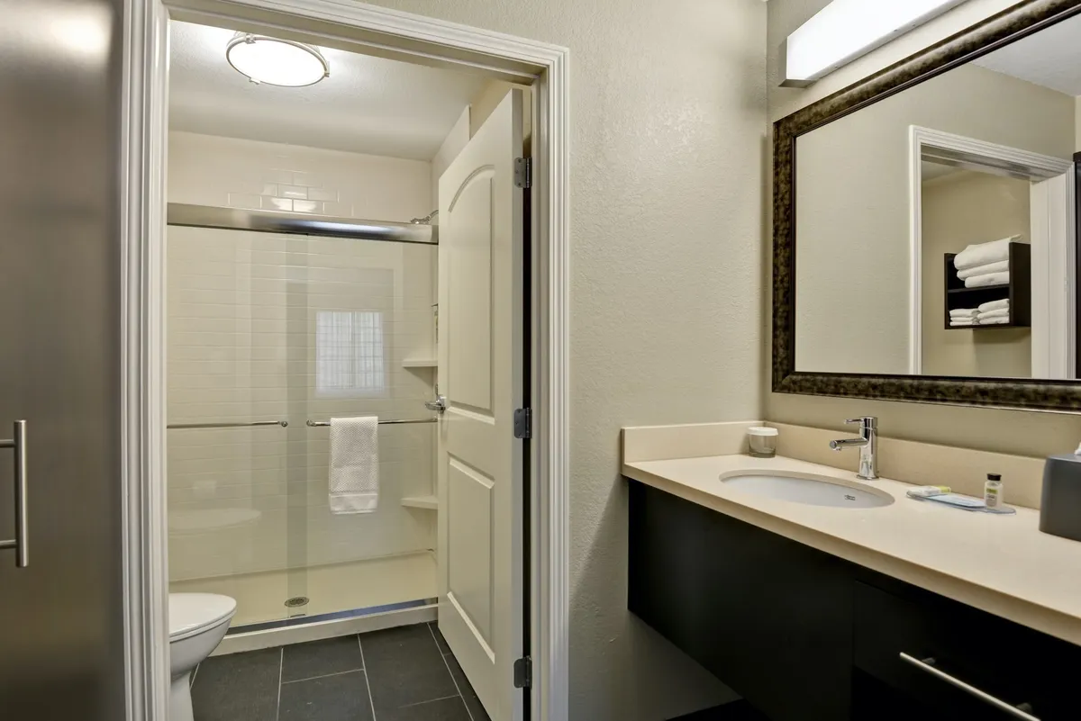 A tranquil bathroom interior featuring a well-lit vanity with a framed mirror, a spacious sink area, and a modern shower. The scene feels serene and inviting, suggesting a private space ideal for personal grooming or unwinding after a long day. Plush towels and complimentary toiletries are subtly visible, heightening the sense of comfort and convenience.