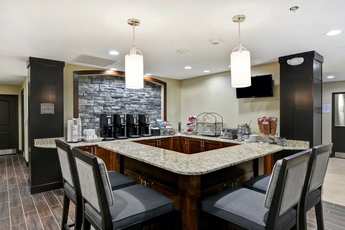 Featuring a granite countertop coffee station adjacent to a communal seating area, this scene highlights morning rituals and social interactions. The stone accent wall and inviting layout suggest a space perfect for starting the day with complimentary breakfast or enjoying evening downtime.