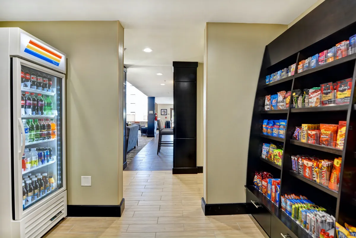 A casual snack display and beverage refrigerator are adjacent to a hallway leading to a cozy seating area. The scene invites guests to grab a treat or drink before relaxing, echoing the convenience of having snacks and refreshments always at hand.